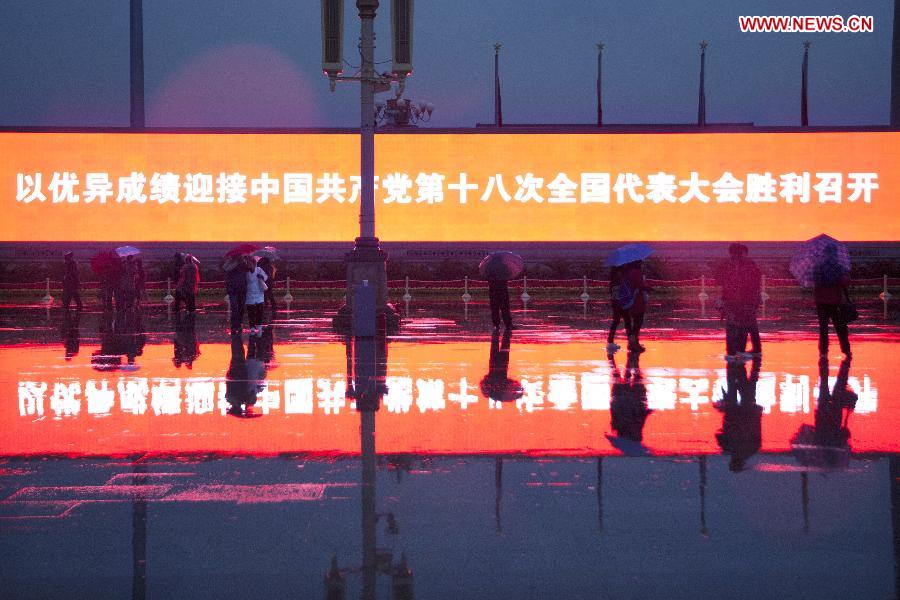 Tourists walk in front of a large electronic board amid rain at the Tian'anmen Square in Beijing, capital of China, Nov. 10, 2012. (Xinhua/Li Gang) 