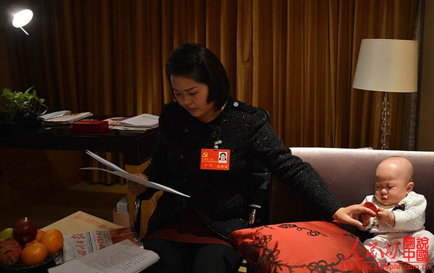 Luo Wei, a deputy to the 18th National Congress of the Communist Party of China, reads material while taking care of her five-month-old daughter in a hotel in Beijing on Nov 10, 2012. (Photo/ People’s Daily Online)