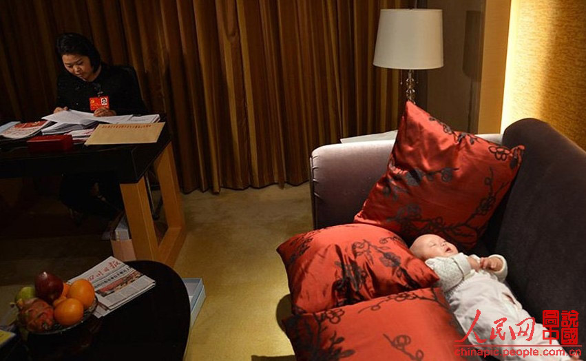 Luo Wei, a deputy to the 18th National Congress of the Communist Party of China, reads material while taking care of her five-month-old daughter in a hotel in Beijing on Nov 10, 2012. (Photo/ People’s Daily Online)