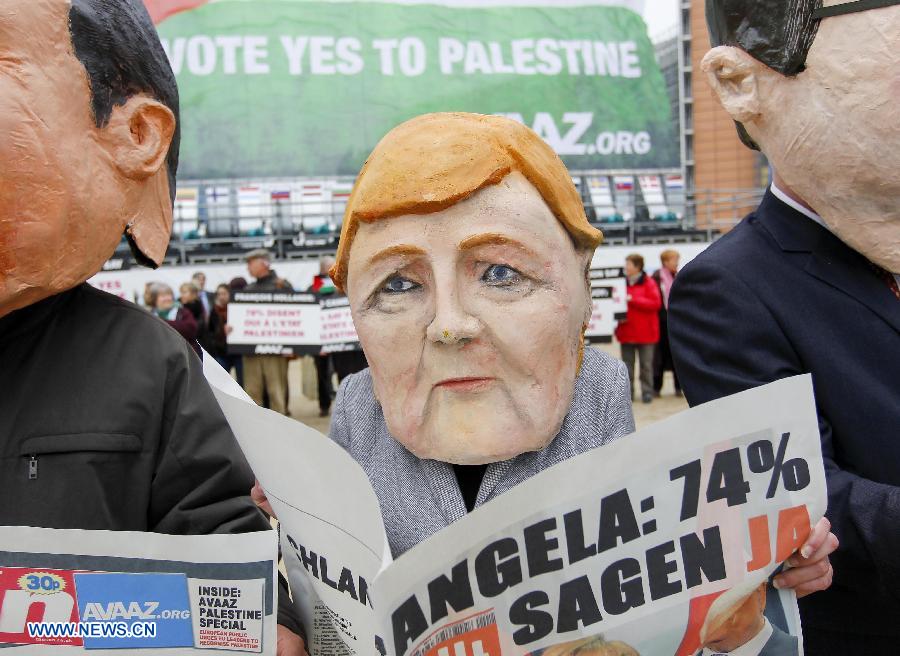 An activist wearing giant heads of German Chancellor Angela attends a rally in front of EU headquarters in Brussels, Belgium, Nov. 19, 2012. Demonstrators installed the giant flag to urge EU backing the Palestinian membership in the United Nations. (Xinhua/Zhou Lei) 