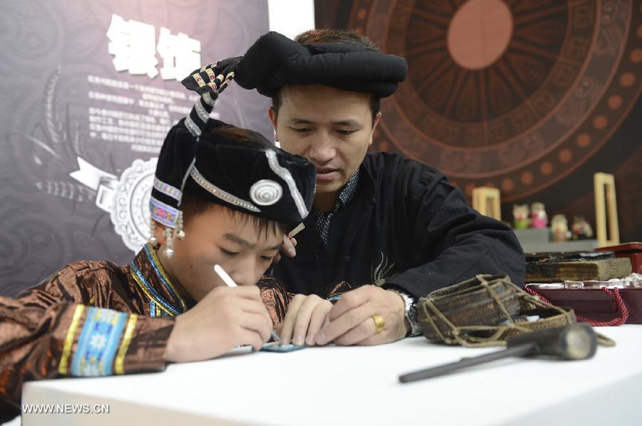 Li Zhengyun (R), the ninth generation of successors for silver-jeweleries-making from Miao ethnic group, instructs his son to make silver ornaments during the show of Guizhou National Folk Handicrafts in Beijing, capital of China, Nov. 21, 2012. (Xinhua/Li Jundong) 