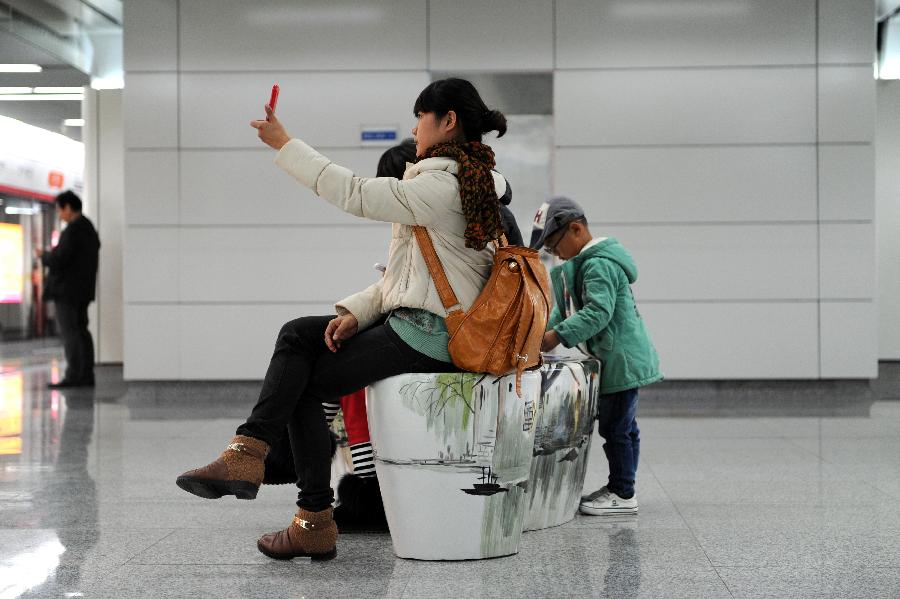 Passengers sit on specially-designed seats with ink paintings inside the Hangzhou Subway Line 1 in Hangzhou, capital of east China's Zhejiang Province, Nov. 24, 2012. Among the 31 stations of the Hangzhou Subway Line 1 which started a trial operation on Saturday, 11 stations were decorated with distinctive art designs. (Xinhua/Ju Huanzong)  