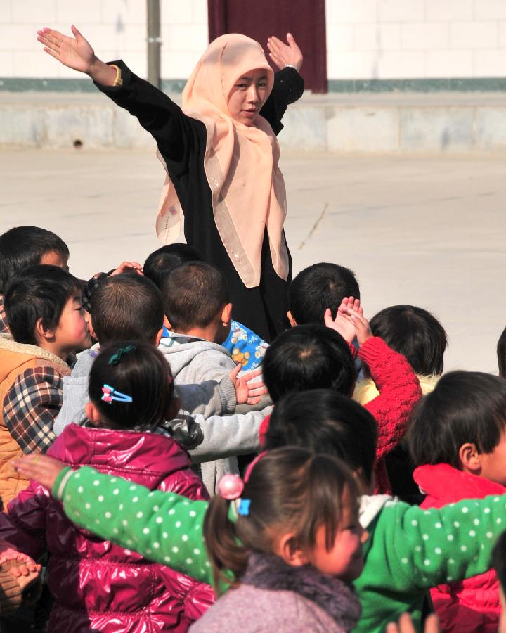 A teacher directs children to do physical exercises at a kindergarten in Dahejia Township of Linxia Hui Autonomous Prefecture, northwest China's Gansu Province, Nov. 29, 2012. A total of 253 children from various ethnic groups study and live at the kindergarten. (Xinhua/Huang Wenxin)