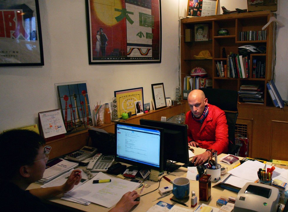 Johnson-Hill (back) looks at computer screen in his office in Beibingmasi alley near Nanluoguxiang of Beijing, capital of China, March 6, 2012.