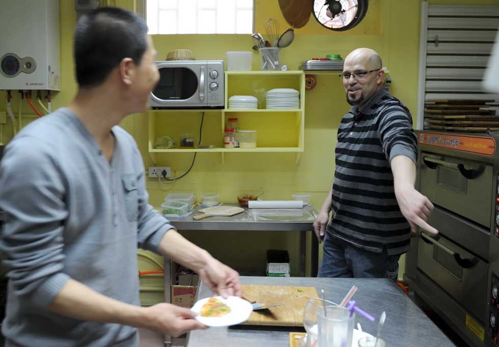 Kevin Gilley (R) talks with a Chinese waiter in the kitchen of his cafe in Dunhuang, northwest China's Gansu Province, April 29, 2012. 