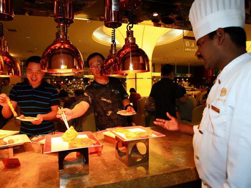 Pandi (1st R) talks to the customers as they taking the roti prata in a buffet restaurant in Hefei, capital of east China's Anhui Province, June 14, 2012. 