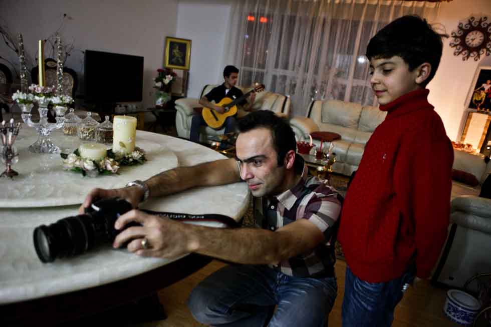 Peyam (L Front) takes pictures with his youngest son Bai Long while Bai Long's brother Bai Yun plays guitar on the sofa at their home in Yinchuan, capital of northwest China's Ningxia Hui Autonomous Region, March 15, 2012.(Xinhua/Zheng Huansong)