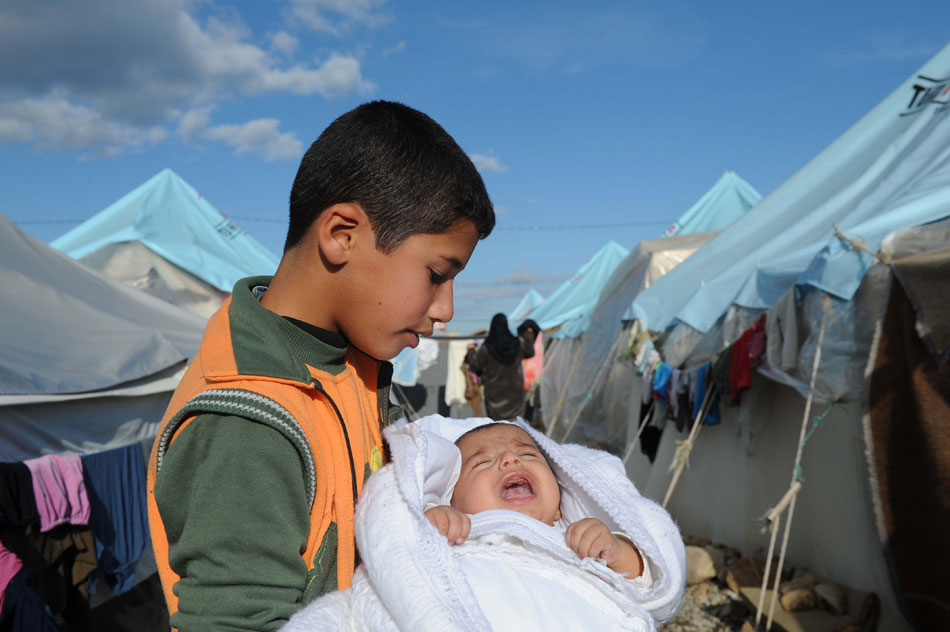 The photo taken on Dec. 8, 2012 shows a Syrian boy holding his younger brother in his arms in a refugee camp, Gaziantep Province, Turkey. (Xinhua/Ma Yan)  