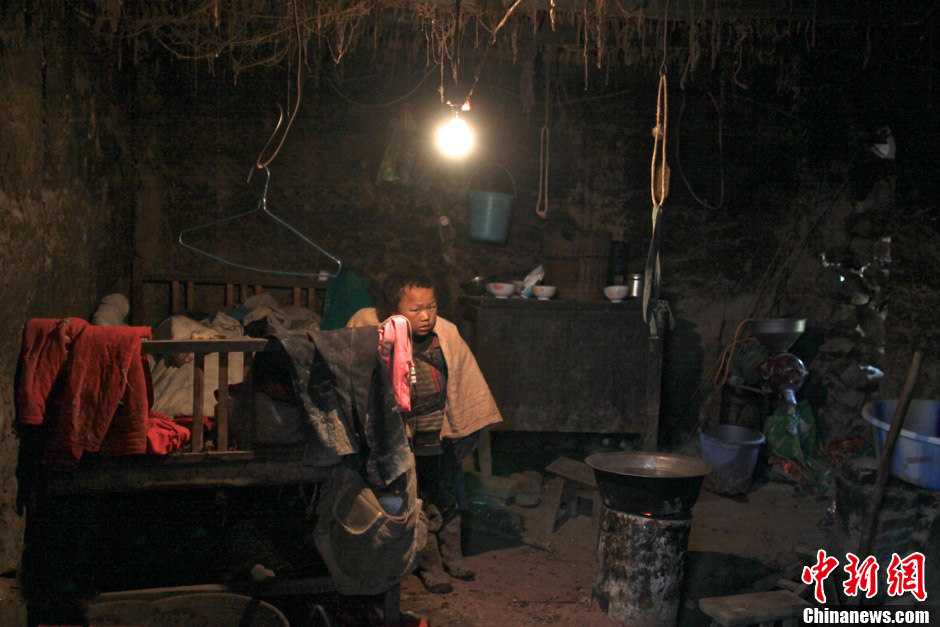 A child with his brother on back hides by the dirty bedside when seeing strangers. (Chinanews/Feng Zhonghao)