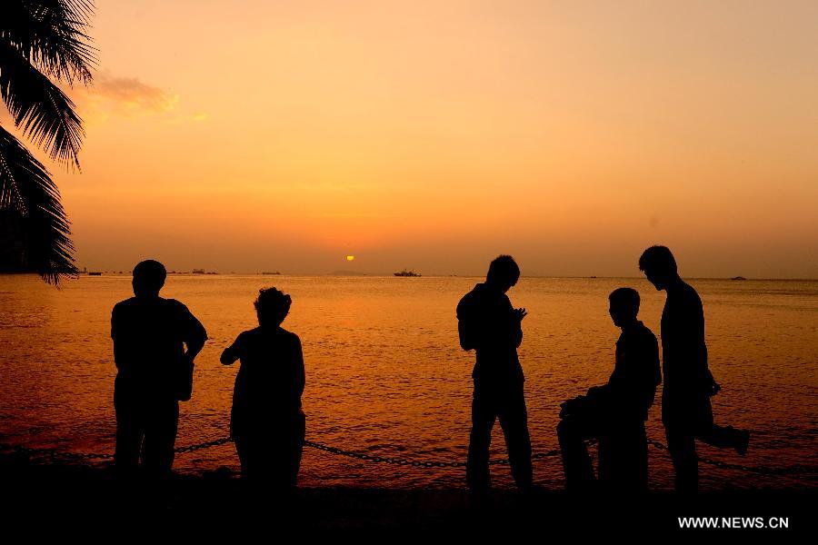 Tourists are silhouetted during the sunset along the Sanya Bay in Sanya, a famous tourism city in South China's Hainan Province, Dec. 25, 2012. (Xinhua/Hou Jiansen)