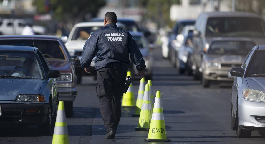 A policeman walks past vehicles whose owners would hand in their guns in Los Angeles, the U.S., on Dec. 26, 2012. Los Angeles police reclaimed guns here on Wednesday in response to the Dec. 14 school massacre in Newtown, Connecticut. Locals who handed in their guns could get cash coupon in return. (Xinhua/Yang Lei) 