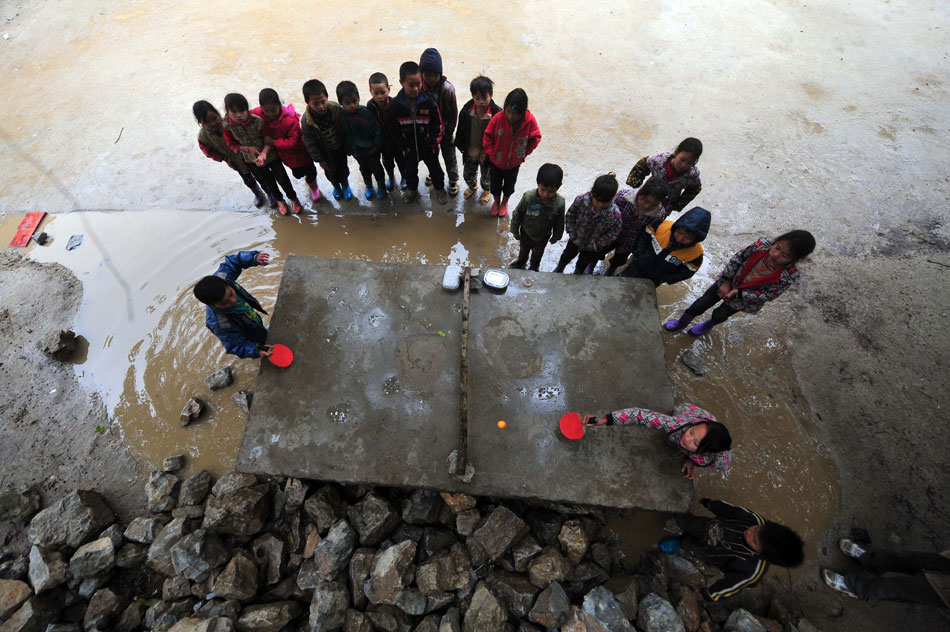 Children stand in a line as they watch a Ping-Pong game taking place on a water-surrounded stone table in a village elementary school, Guangxi Zhuang Autonomous Region, Dec. 27, 2012. (Xinhua/Huang Xiaobang)