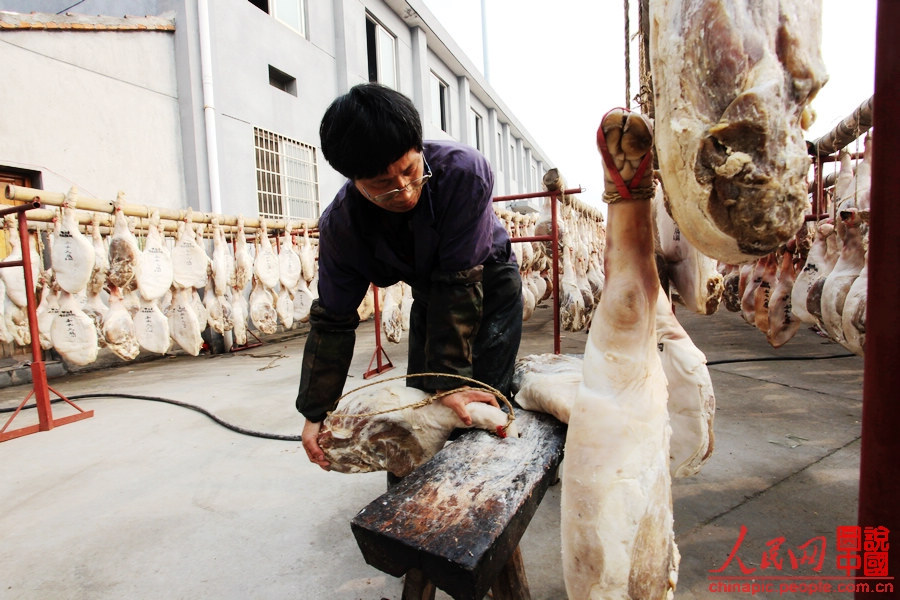 The worker shapes the ham by pickling it into the hold of the bench and straightening it.