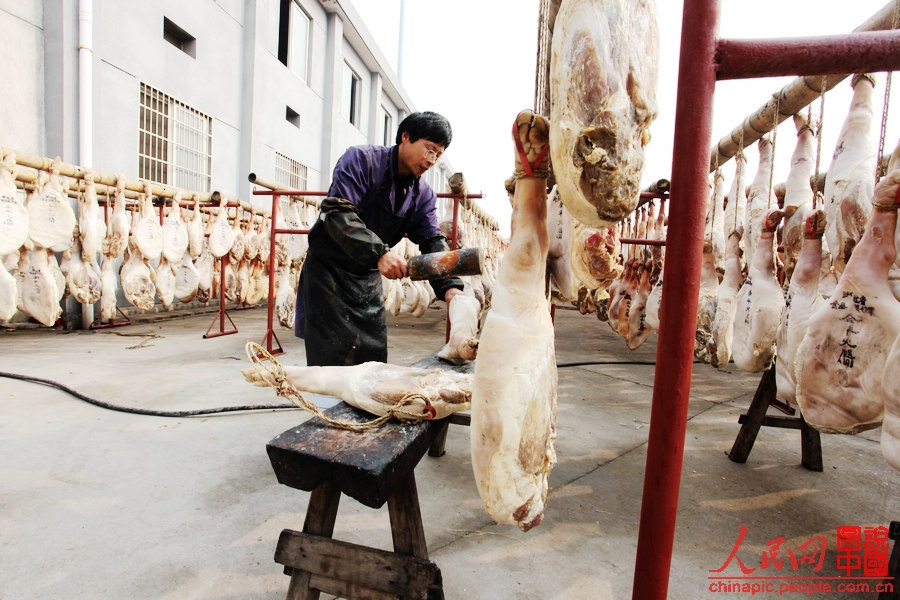 The worker shapes the ham by hitting it with a wooden hammer.