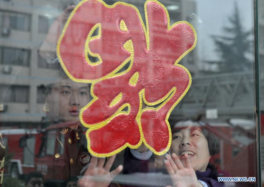 Hao Min (R), a community worker, attaches a paper-cut ornament in the shape of Chinese character "Fu", or happiness in English, onto windows together with firefighter Han Xiaoyu at a fire brigade in Wulidun Community of Hefei, capital of east China's Anhui Province, Jan. 30, 2013. A group of community workers and retired staff members visited Wulidun fire brigade to celebrate the upcoming Spring Festival with the firefighters here on Wednesday. (Xinhua/Guo Chen) 