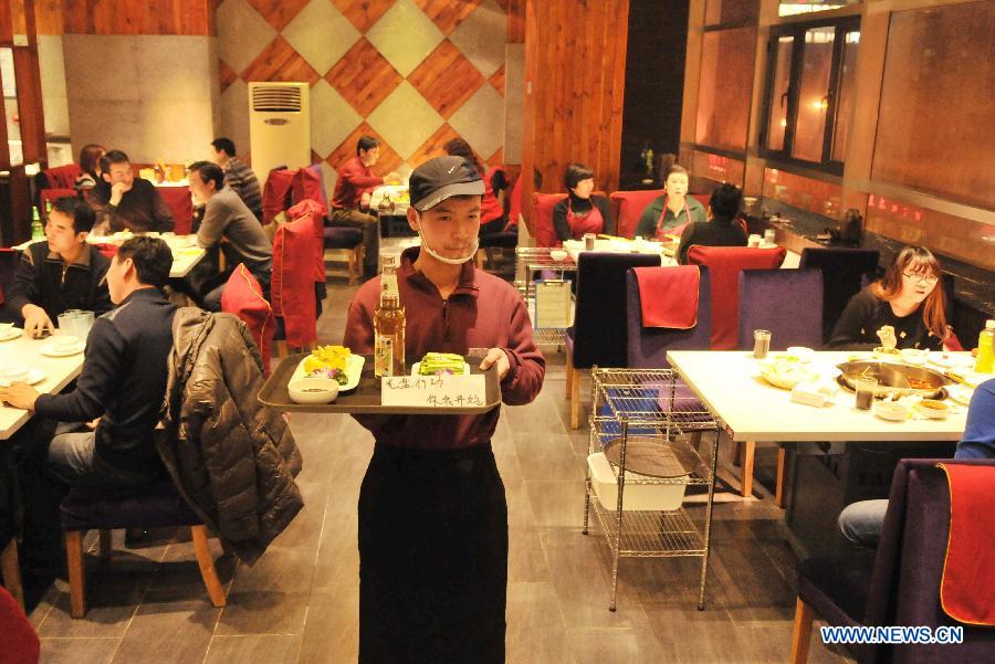 A working staff serves the dishes at a hot pot restaurant in Lanzhou, capital of northwest China's Gansu Province, Jan. 30, 2013. A "half portion, half price" activity was launched by numerous hot pot restaurant to advocate saving here Wednesday. (Xinhua/Chen Bin)