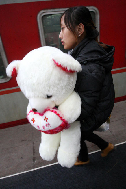 A woman boards a train with a toy bear at Yantai Railway Station in East China's Shandong province on Feb 3, 2013.(Photo/Xinhua)