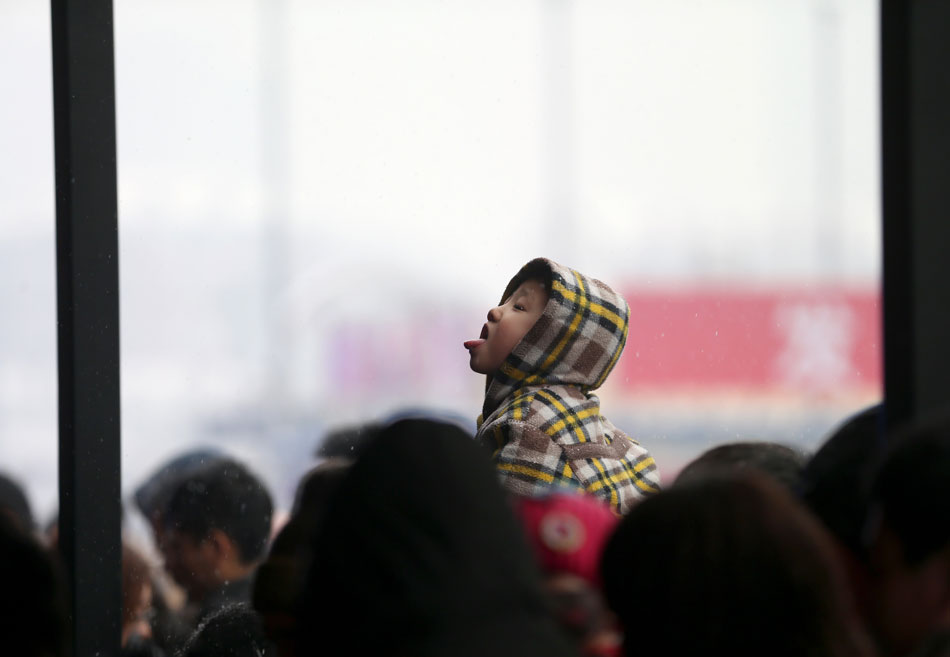 A toddler tries to taste snowflake on father’s shoulder at Beijing Railway Station, Feb. 3. (Xinhua/Jin Liwang)