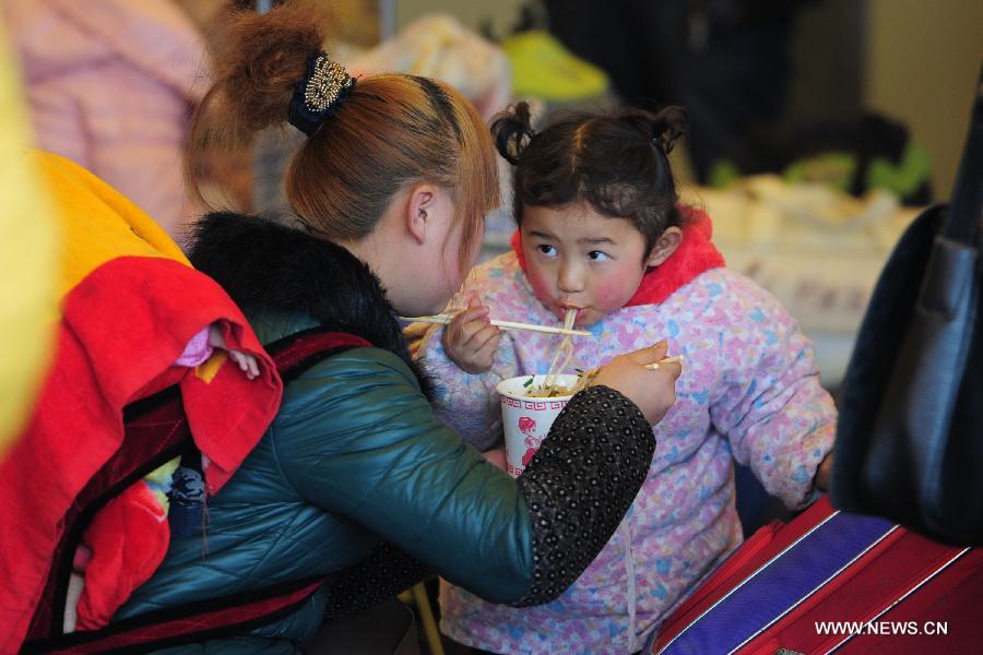 A woman feeds rice noodle to her daughter at the Guiyang Railway Station in Guiyang, capital of southwest China's Guizhou Province, Feb. 17, 2013. When the Spring Festival holiday comes to an end, migrant workers start to leave their hometowns in Guizhou for job opportunities in China's more affluent coastal provinces. Many have to take their children with them. (Xinhua/Liu Xu)