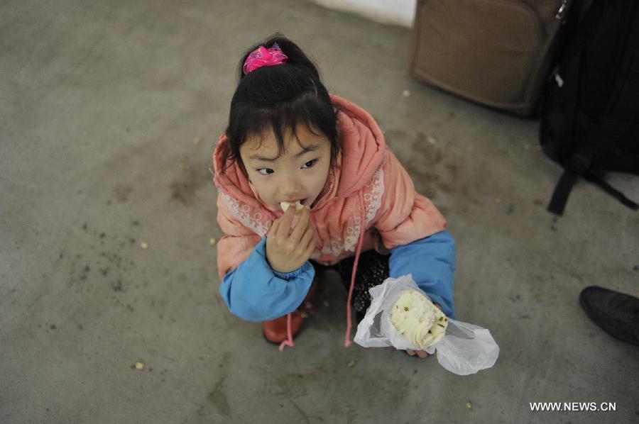 A girl eats food while waiting for her bus at Jinyang bus station in Guiyang, capital of southwest China's Guizhou Province, Feb. 17, 2013. Migrant workers, together with their children, started to return to the urban areas to work after the one-week Spring Festival holiday ended. (Xinhua/Ou Dongqu)