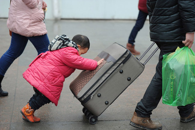 A girl helps her parents to push luggage at the railway station in Guiyang on Feb. 17, 2013. After the end of Spring Festival holiday, many migrant workers, along with their children, left hometown to seek better job opportunities in big cities.  (Photo/Xinhua)