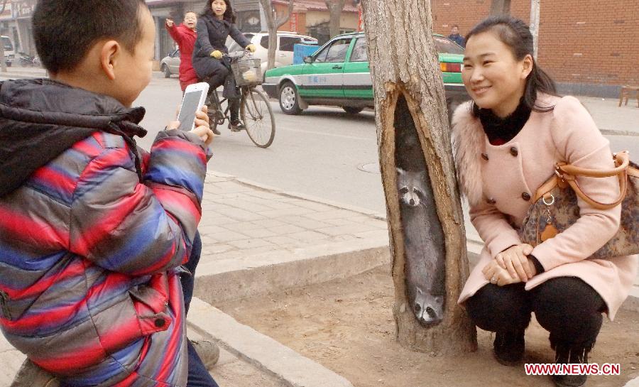 A local resident poses for a photo beside a tree hollow painting at Jiuzhong street in Shijiazhuang, capital of north China's Hebei Province, Feb. 24, 2013. Paintings in shade tree hollows by Wang Yue, a local art student, became an Internet sensation lately. (Xinhua/Ding Lixin)