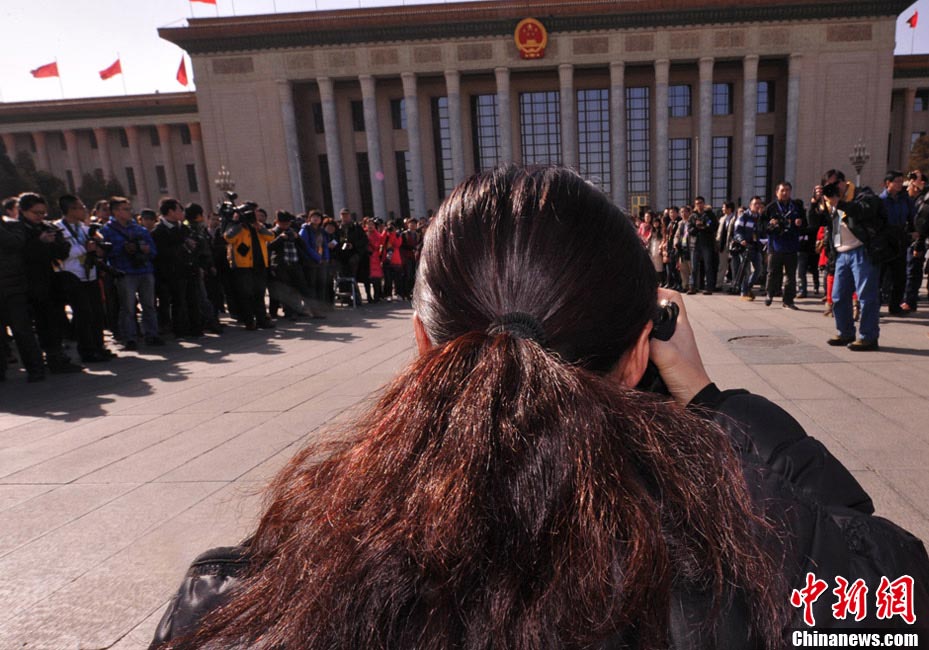 A female journalist covering the NPC and CPPCC sessions takes photos. (Photo/CNS)