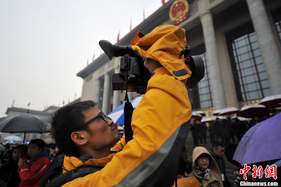 Photo shows a reporter covering the news in the rain. On March 12 Beijing received the first rainfall of the year as 12th National Committee of the Chinese People's Political Consultative Conference concluded its first session. (Chinanews.com/ Jin Shuo)