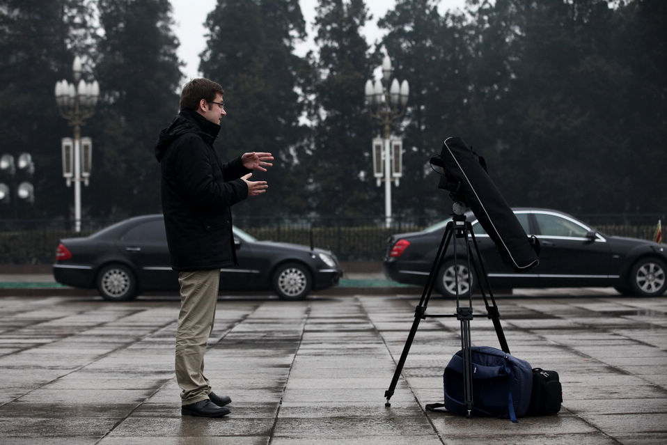A foreign journalist who is in live report protects the camera with his bag from the rain. The closing meeting of the first session of the 12th National Committee of the Chinese People's Political Consultative Conference (CPPCC) was held on Tuesday. On the same day, Beijing embraced the first spring rain in 2013. (Xinhua News Agency/Liu Jinhai)