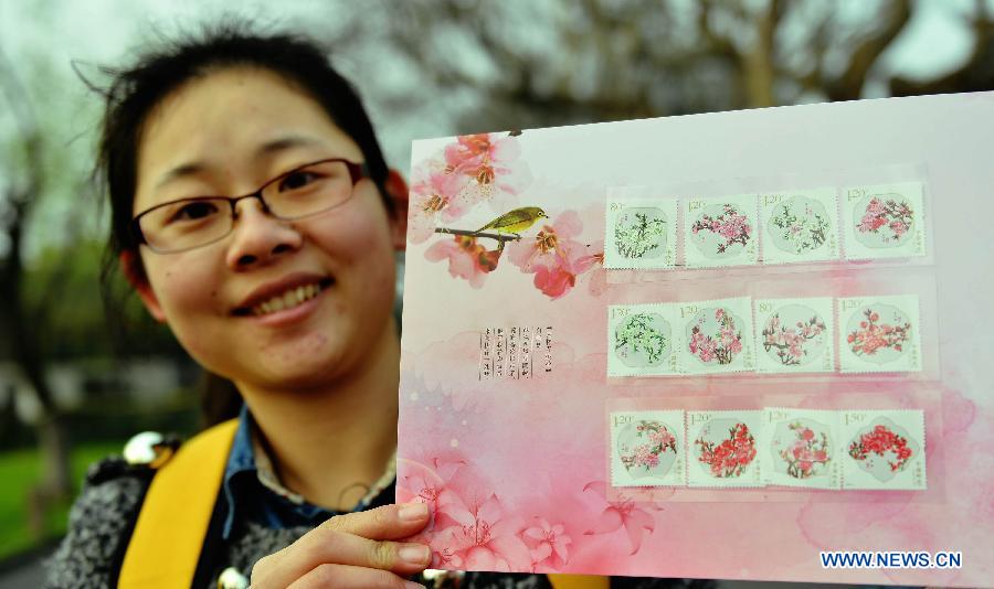 A stamp collector presents the "peach blossom" stamps at the West Lake in Hangzhou, capital of east China's Zhejiang Province, March 16, 2013. China Post published a set of "peach blossom" stamps on Saturday. (Xinhua/Long Wei)  