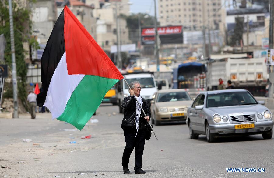 A female Palestinian protester raises a national flag in front of Israeli soldiers at Qalandiya checkpoint near the West Bank city of Ramallah on March 30, 2013. Land Day commemorates the killing of six Palestinians by Israeli security forces in 1976 during a protest against the expropriation of their lands by the Israeli government in the northern Galilee region. (Xinhua/Fadi Arouri)