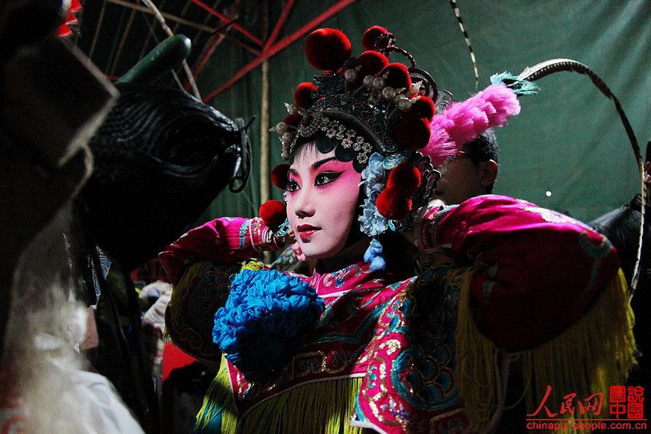 A staff member helps Yang Xiayun wear heavy and delicate head crest and other accessories before performance.