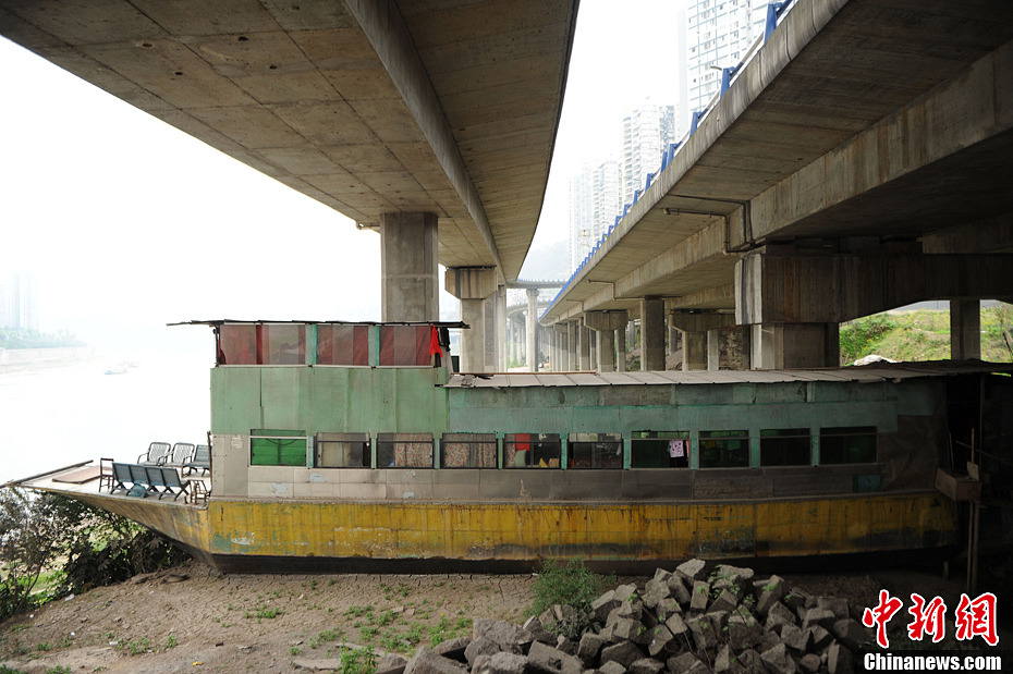 A family lives in a 10-meter-long fishing smack that is aground beside a pier of the bridge over Jialing River in Chongqing city. (Photo by Chenchao/ Chinanews.com)