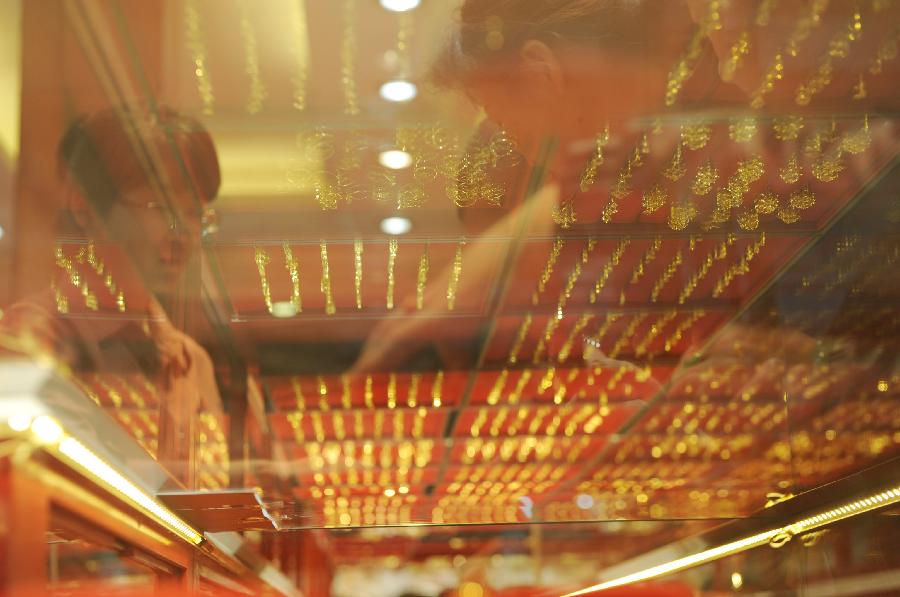 Image of coustomers is reflected on the glass counter at a gold jewellery shop in Wuxi, east China's Jiangsu Province, April 18, 2013. Gold jewellery shops through China have lowered price of gold jewellery due to the consecutive decline of gold price global markets recently, which boost sales in these shops. (Xinhua/Zhang Liwei) 