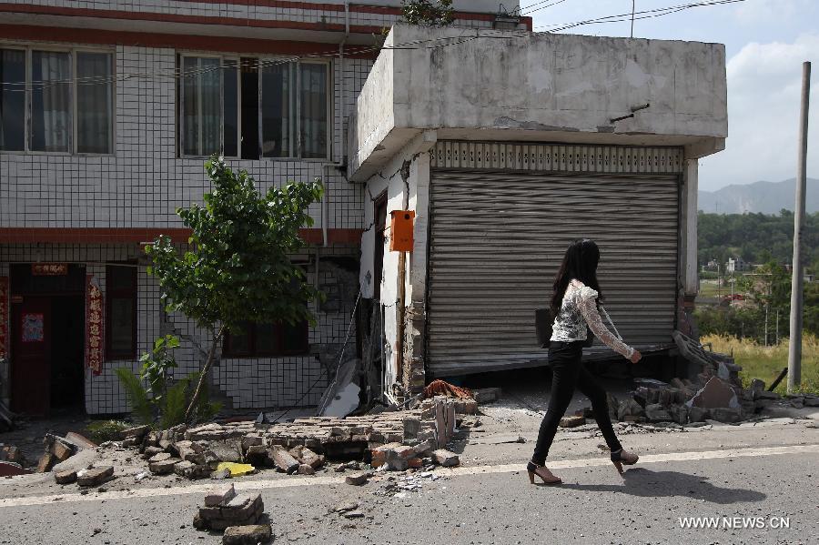 A woman passes by a house damaged by a 7.0-magnitude earthquake in Longmen Township, Lushan County, Ya'an City of southwest China's Sichuan Province, April 20, 2013. At least 102 people were killed in the earthquake in Sichuan, according to the China Earthquake Administration on Saturday afternoon. (Xinhua/Zhang Xiaoli)  