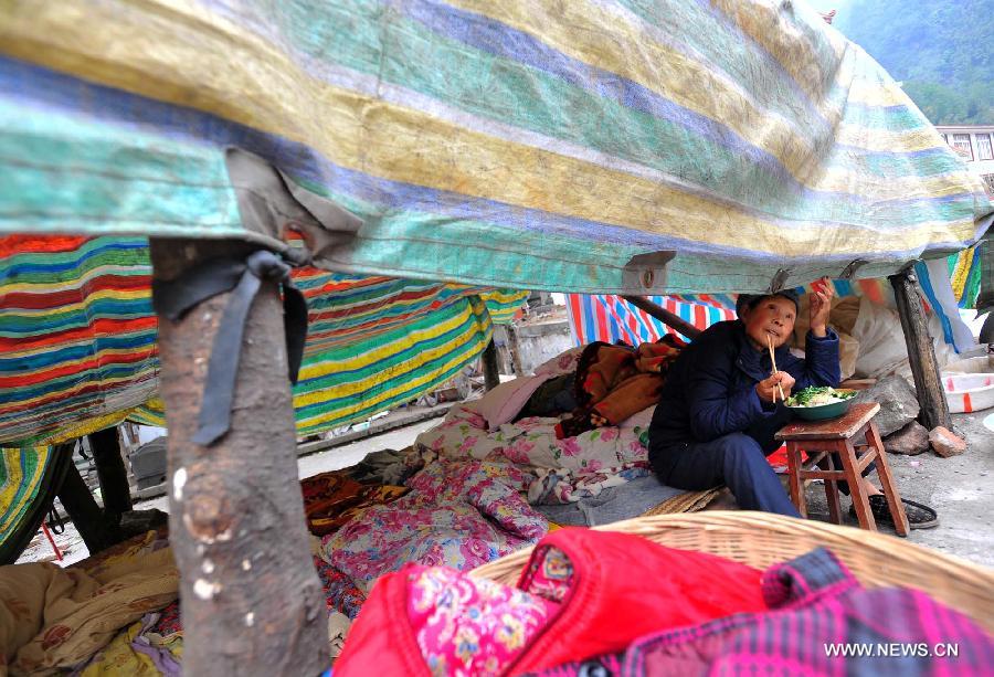 A villager has a meal in a makeshift tent in Baosheng Township, Lushan County, southwest China's Sichuan Province, April 21, 2013. Baosheng Township is another seriously affected area in Lushan. Search and rescue work continued here Sunday, and the work for restoring roads and communications are conducted in the pipelines. (Xinhua/Xiao Yijiu)