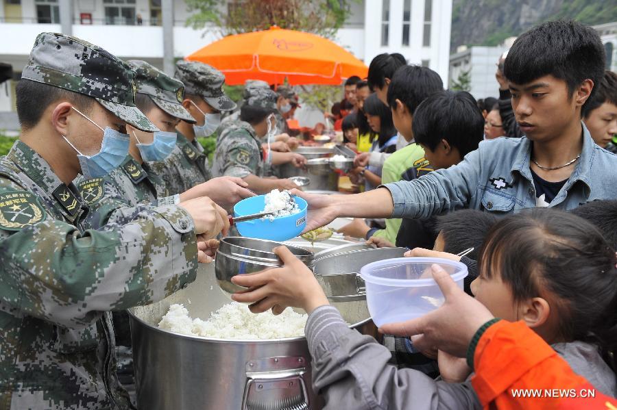 Soldiers distribute food for students at a school served as an evacuation settlement for displaced people in the quake-hit Baoxing County, southwest China's Sichuan Province, May 2, 2013. Some 4,000 displaced people live the settlement, the largest in the county, after a strong earthquake hit Baoxing last month. At present, basic living needs of those people could be guaranteed in terms of food, drink, healthcare service and power supply. (Xinhua/Lu Peng)