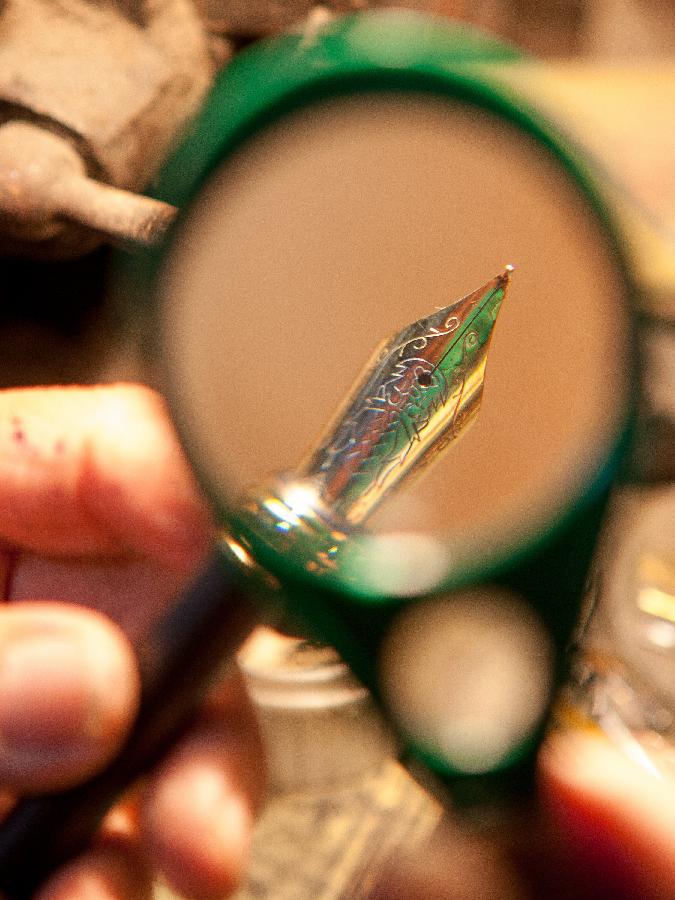 Zhang Guangyi examines a pen tip with a magnifier at his shop in Beijing, capital of China, April 26, 2013. (Xinhua/Xu Zijian)