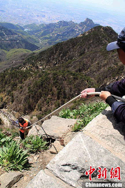 Zhang’s workmate tightly holds the rope that is tied round Zhang’s waist. (Photo by Li Xianglei/ Chinanews.com)