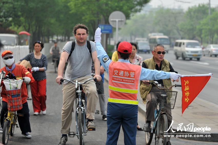 Cyclists follow traffic warden’s direction at a crossing in Beijing, May 6, 2013. (Weng Qiyu /People’s Daily Online)