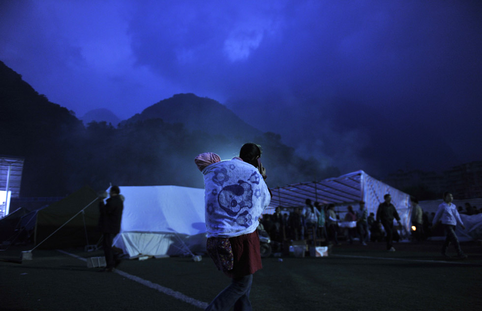 A woman carrying her baby on her back makes a phone call outside a temporary tent for quake victims in the darkness. Photo taken by Chen Yuxiao is released by Xinhua on April 28, 2013.