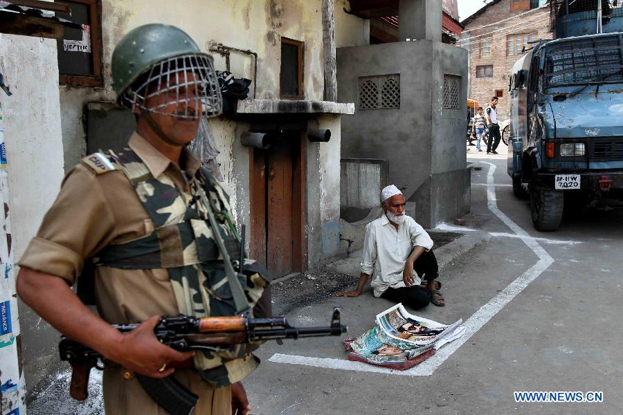 A vendor sits on a pavement selling posters, as a paramilitary guard stands guard outside the separatist party's office in Srinagar, Indian-controled Kashmir, on May 21, 2013. A shutdown called by separatists to mark the anniversaries of two killed separatist leaders Mirwaiz Muhammed Farooq and Abdul Gani Lone was observed here on Tuesday. Authorities have placed moderate separatist leader Mirwaiz Umar Farooq under house arrest. (Xinhua/Javed Dar)