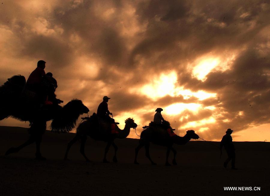 Tourists ride on camels visiting the scenic spot of the Mingsha Mountain and Crescent Spring in Dunhuang City, northwest China's Gansu Province, May 21, 2013. Dunhuang has received about 749,200 tourists in the first four months of 2013, increasing 58.63 percent year on year. (Xinhua/Nie Jianjiang)  