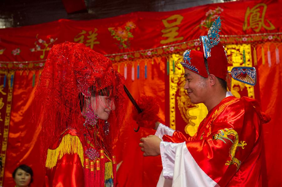 Bridegroom Zhang Lan (R) unveils for his Russian bride Ren Niya (her Chinese name) during the wedding ceremony in a courtyard dwelling in Chongqing, southwest China, May 23, 2013. The wedding ceremony, held in the traditional Chinese way, attracted lots of passengers to give their blessings. (Xinhua/Chen Cheng)