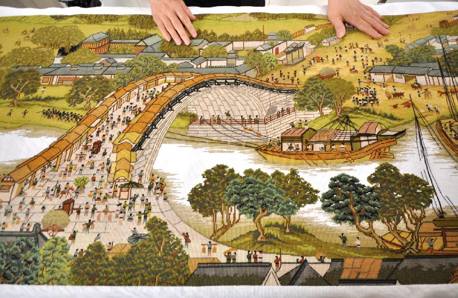 Yang Hua demonstrates the 22-meter-long cross-stitch work of "Riverside Scene at the Qingming Festival" in Yiyuan County, east China's Shandong Province, May 22, 2013. Yang spent more than three years to finish the cross-stitch. (Xinhua/Zhao Dongshan) 