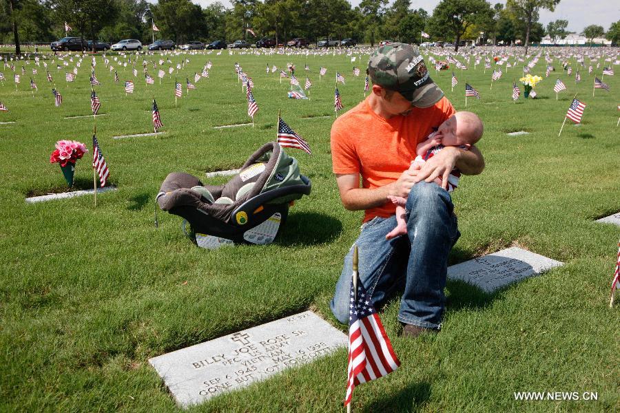 Billy Rose Jr mourns for his father holding his six-month-old son on the Memorial Day at the Houston National Cemetery in Houston, the United States, May 27, 2013. (Xinhua/Song Qiong) 