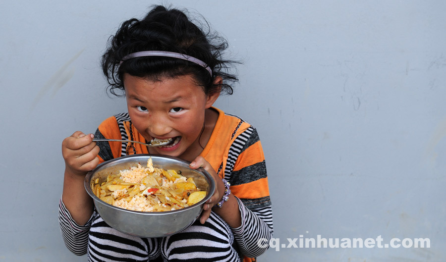 A junior student has his meal against the wall at lunch time since there’s no cafeteria at school. (Photo by Huang Junhui/ cq.xinhuanet.com)