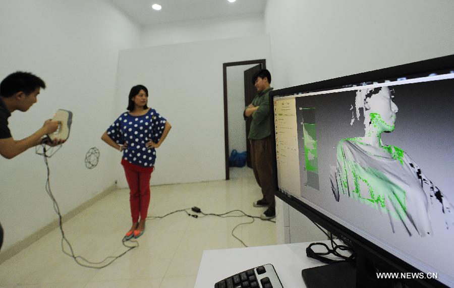 A staffer scans a young couple to make 3D-printed figurines at a newly-opened 3D printing gallery in Chongqing, southwest China's municipality, June 3, 2013. (Xinhua/Li Jian)