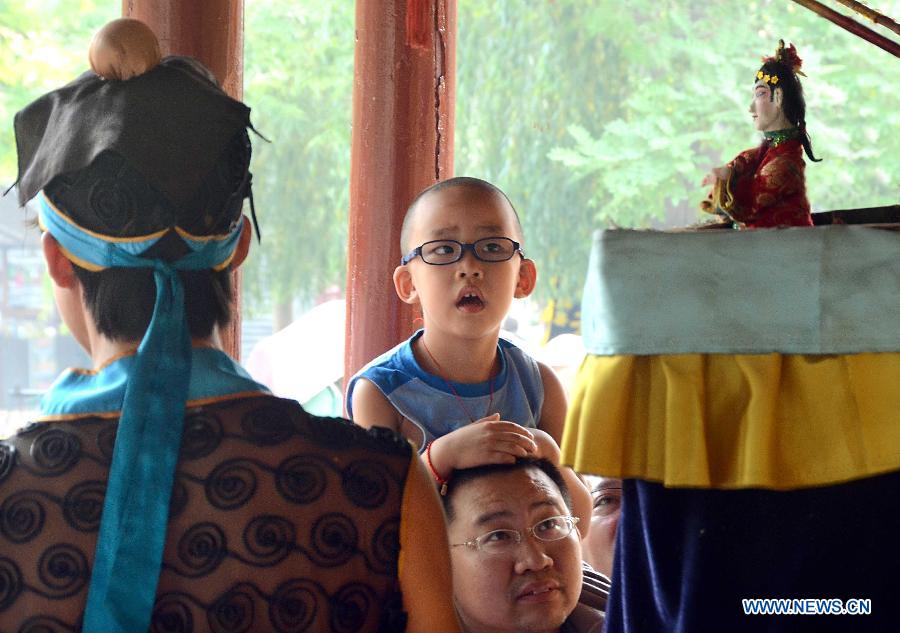 A boy sitting on an adult's shoulders watches puppet show on the Cultral Week for the annual Dragon Boat Festival in Kaifeng, central China's Henan Province, June 9, 2013. The week-long event, which was kicked off here Sunday, will held a series of activities of folk custom, showcasing local intangible cultural heritage to tourists. (Xinhua/Wang Song)