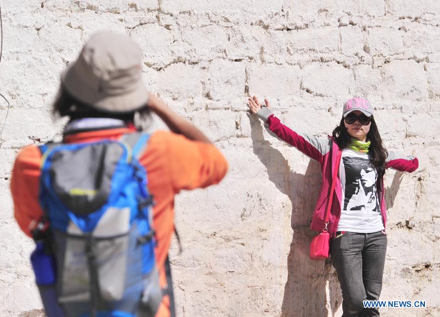 A visitor poses for photos outside the Jokhang Temple in Lhasa, capital of southwest China's Tibet Autonomous Region, June 4, 2013. Lhasa has accepted more than 1 million people from January to May in 2013 and witnessed a tourism income of 1.033 billion yuan (about 165.28 million U.S. dollars ), making year on year increase of 35.86 percent and 49.35 percent respectively. (Xinhua/Liu Kun)